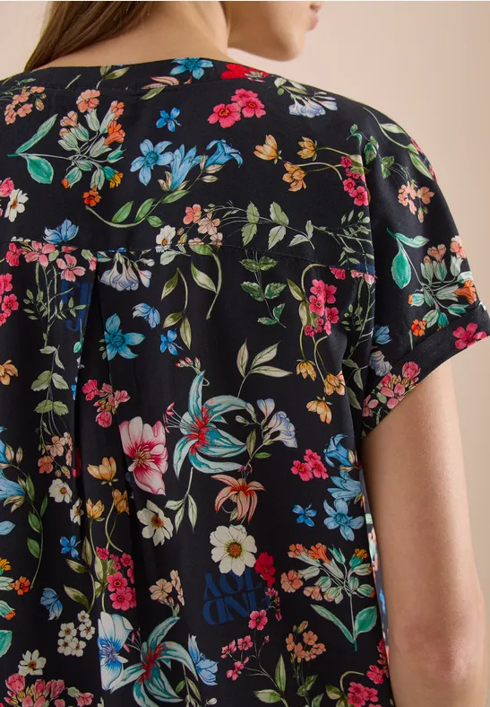 Rückenansicht einer Frau in kurzärmligem schwarzem Shirt mit farbenfrohem Blumenmuster.