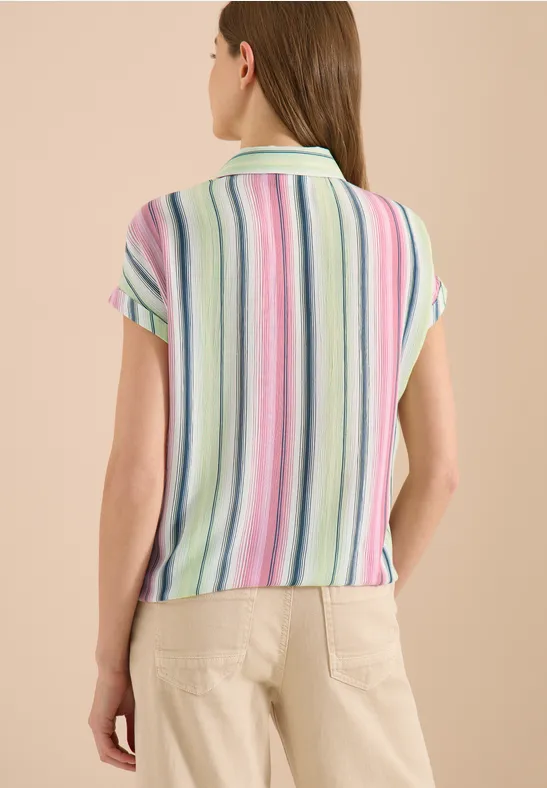Vrouw van achteren in een kort mouwpolo met pastelkleurige strepen en een lichtgekleurde broek.