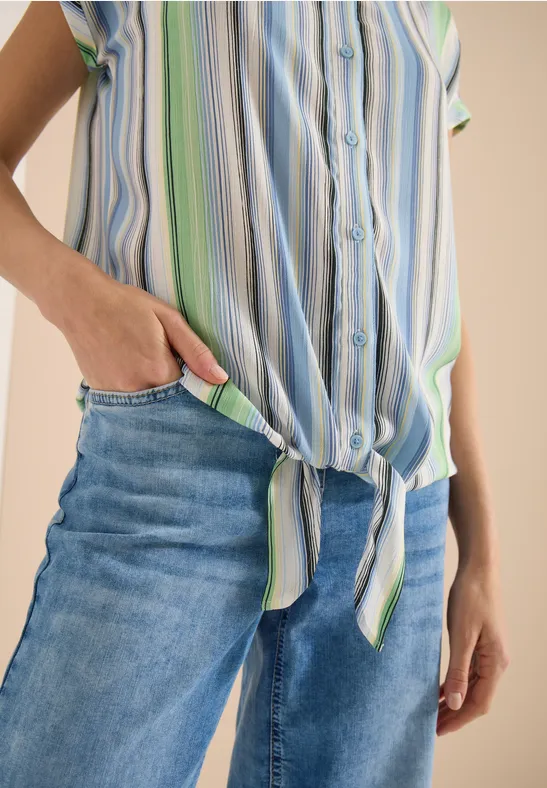 Person trägt blaue Jeans und gestreiftes Hemd, geknotet an der Taille, Hand in Tasche.