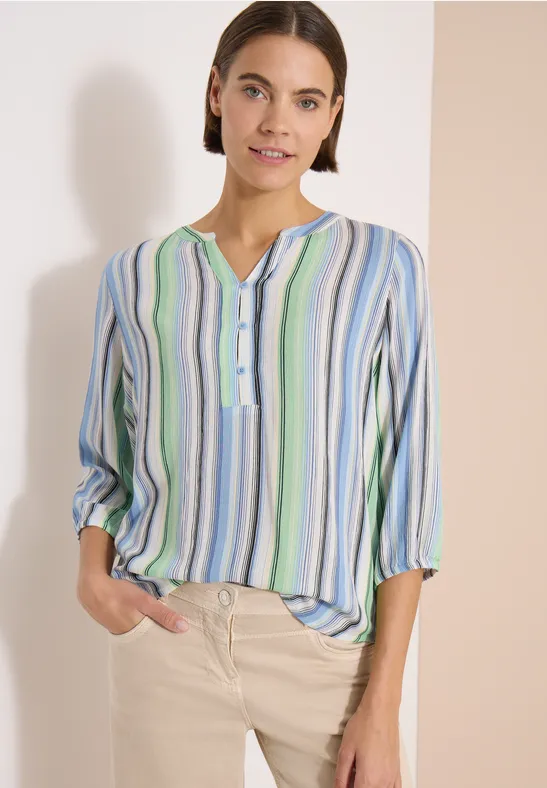 Femme porte une blouse rayée bleu, vert et blanc, col V et patte de boutonnage.