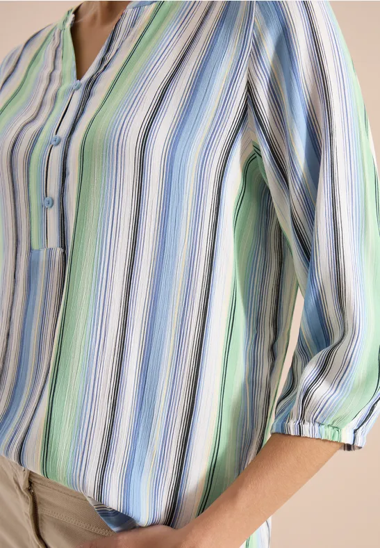 Une personne porte un chemisier pastel rayé aux manches 3/4 retroussées, associé à un pantalon beige.