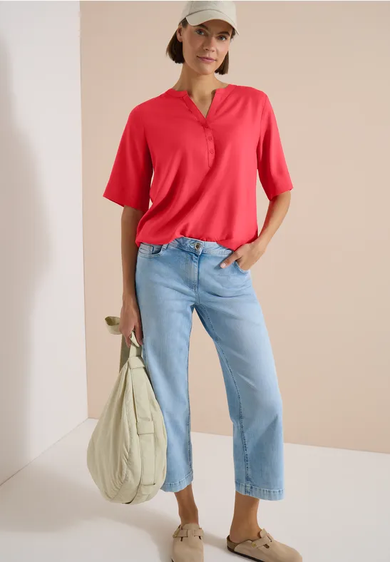 Person trägt rotes Poloshirt, blaue Jeans und beigen Stoffbeutel.