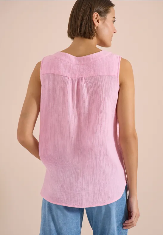 Rückansicht einer Frau in ärmellosem rosa Top und blauen Jeans vor hellem Hintergrund.