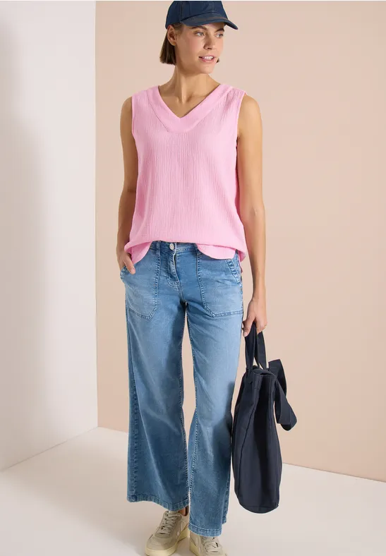 Frau in pinkem V-Ausschnitt-Top und weiten Jeans hält navyblauen Beutel.