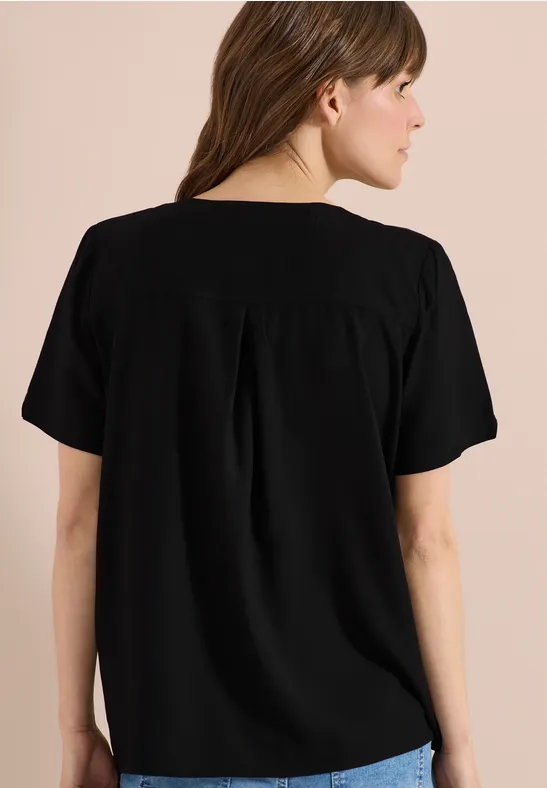 Rugaanzicht van een vrouw in een zwart shirt met korte mouwen voor een neutrale achtergrond.