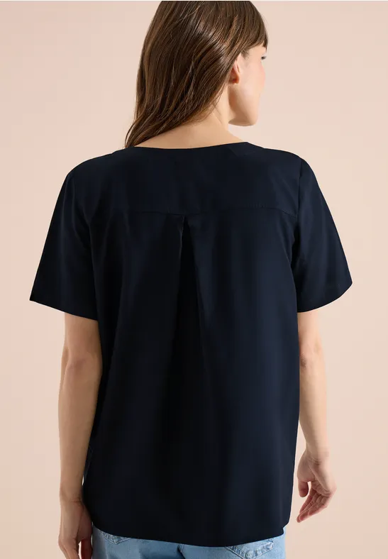 Rugbeeld van een vrouw in losvallend donkerblauw shirt met korte mouwen