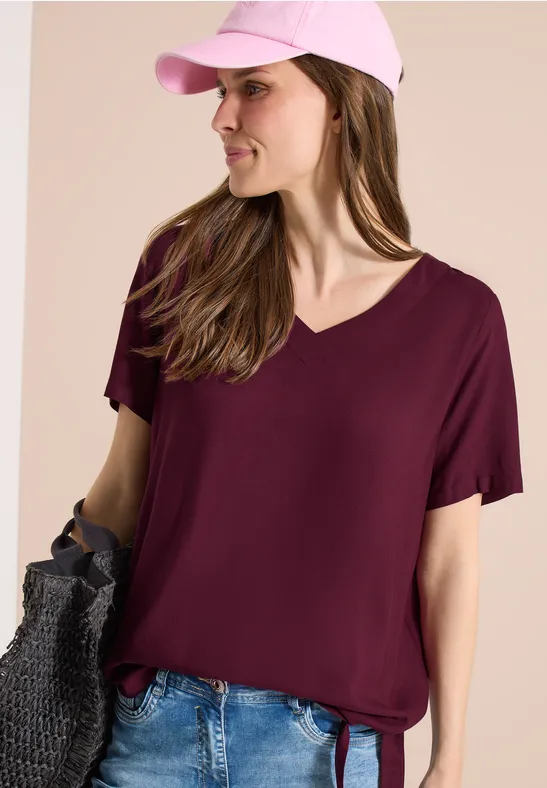 Frau trägt weinrotes V-Ausschnitt-T-Shirt mit kurzen Ärmeln und Jeans.