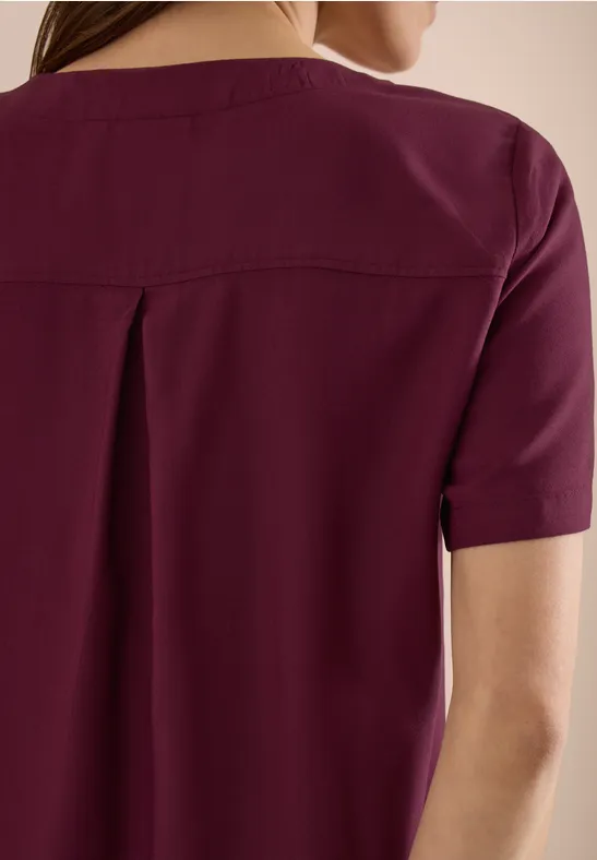 Frau von hinten in einem kurzärmeligen burgunderfarbenen Oberteil.