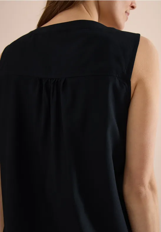 Rückansicht einer Frau in einem ärmellosen, schwarzen Top mit dezenter Rückenfalte.