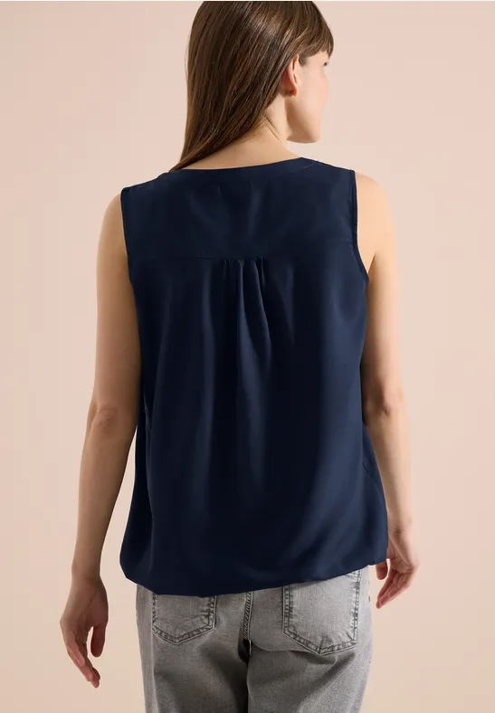 Rückenansicht einer Frau in navy ärmelloser Bluse und grauer Jeans.