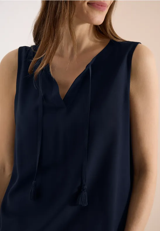 Frau in dunkelblauem, ärmellosem Top mit V-Ausschnitt und Quastenbändern