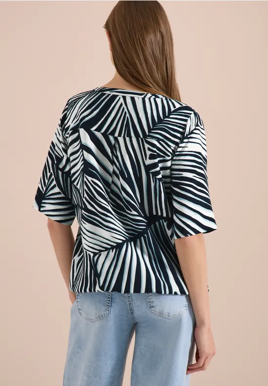 Frau trägt schwarz-weiße Zebramusterbluse mit Rückenknoten und blauen Jeans.