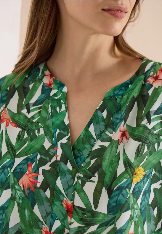Vrouw met groen bovenstuk met tropische bladprint en rode en gele bloemen, V-hals.