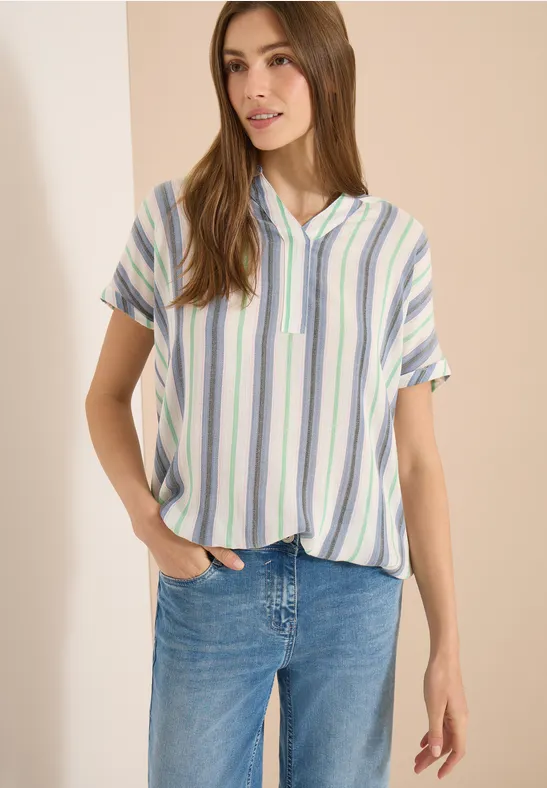 Frau in kurzärmligem, pastellgestreiftem Hemd und blauen Jeans.
