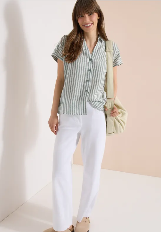 Eine Person trägt grünes, gestreiftes Kurzarmhemd, weiße Hose und trägt eine Handtasche.
