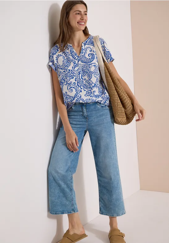 Vrouw met blauw-wit motief blouse, wijde jeans, nude pumps en gevlochten tas.
