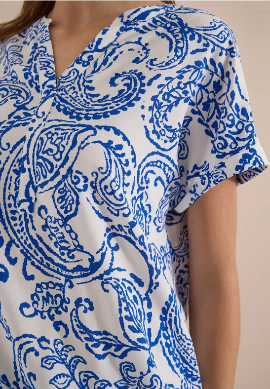 Witte top met blauw paisley-patroon en korte mouwen.