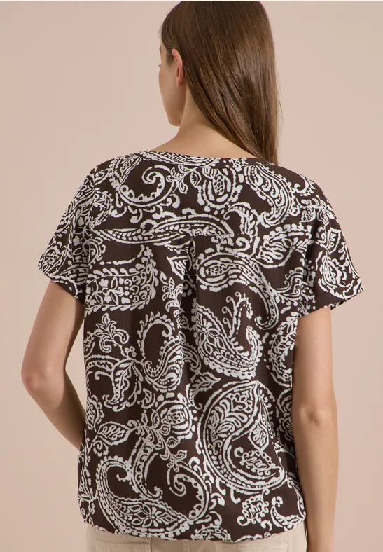 Achteraanzicht van een vrouw in een loszittend zwart-wit paisley-print T-shirt met korte mouwen.