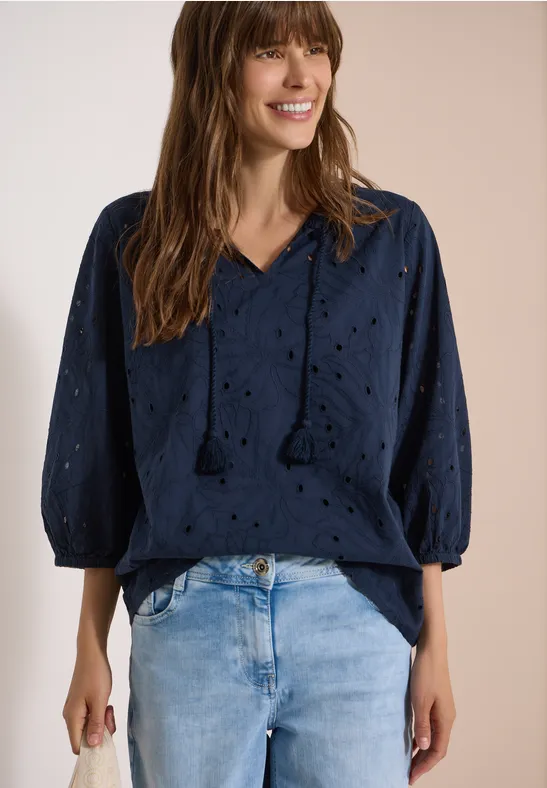 Frau trägt dunkelblaue Lochstickerei-Bluse mit V-Ausschnitt und Jeans.