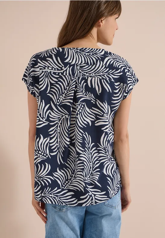 Achteraanzicht van een vrouw in een blauw-wit bladprint T-shirt met korte mouwen en een spijkerbroek.