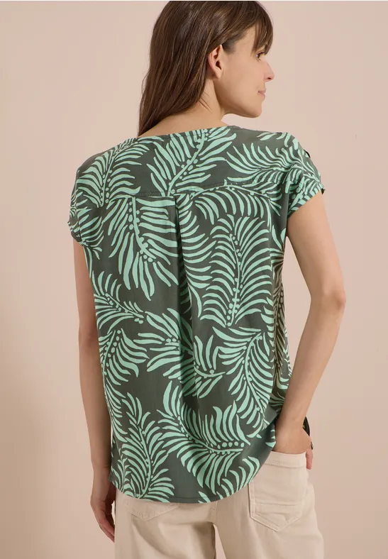 Vrouw van achteren in groene top met bladerenpatroon.