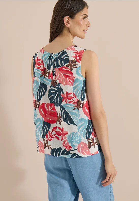 Vrouw van achteren in een mouwloze top met kleurrijke bladprint en wijde blauwe broek.