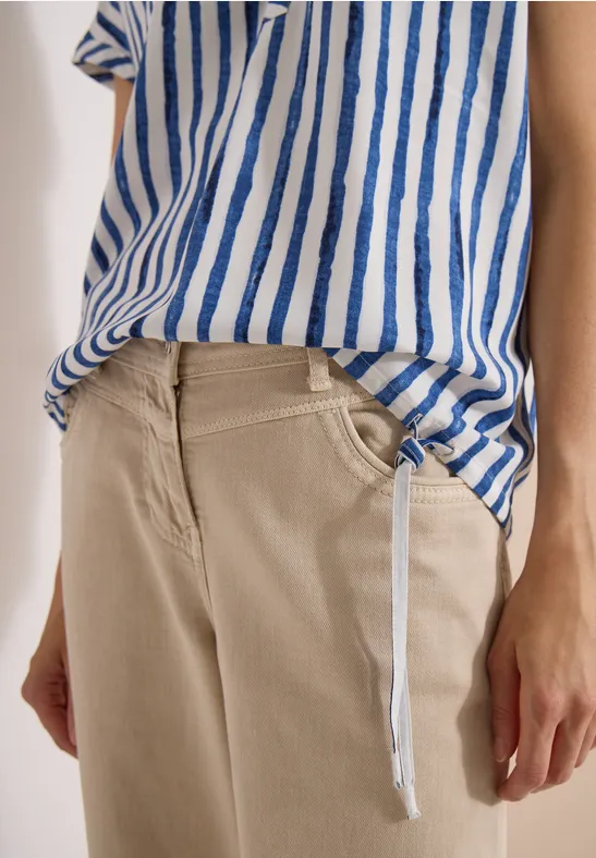 Person trägt beige Hose und blau-weiß gestreiftes Shirt, sichtbare Hände und ein hängender Kordelzug.