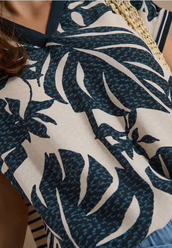 Nahaufnahme einer Bluse mit dunkelblauem Monstera-Blättermuster auf beigem Hintergrund.