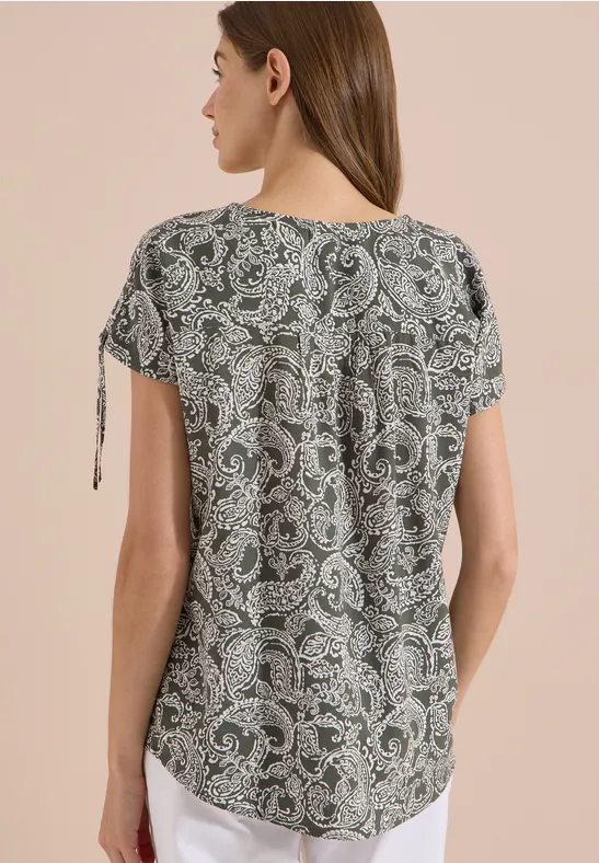Vrouw van achteren in een losvallend t-shirt met korte mouwen, paisleyprint en sierstrikjes bij de mouwen