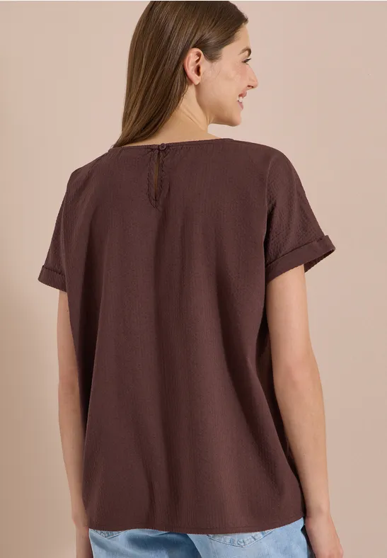 Rugaanzicht van een vrouw in een eenvoudig bruin T-shirt met omgeslagen mouwen.
