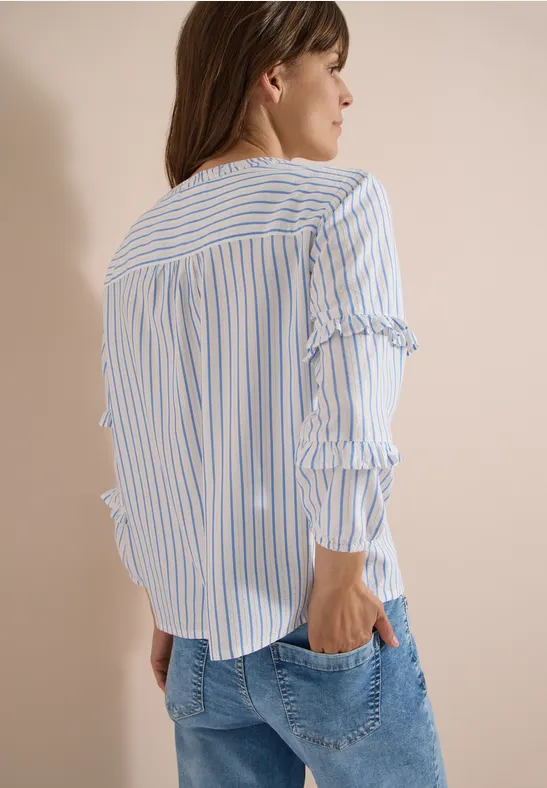 Frau von hinten in blau-weiß gestreifter Bluse mit Rüschenärmeln und Jeans.