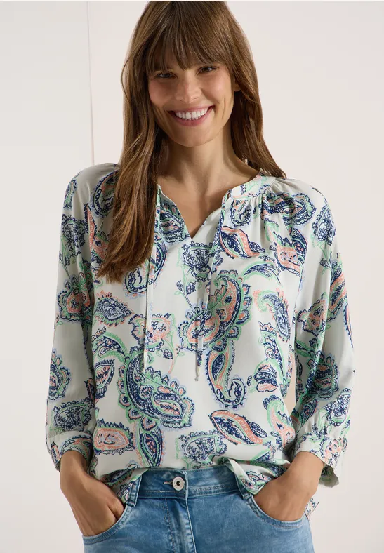 Eine Frau trägt eine Bluse mit buntem Paisley-Muster und V-Ausschnitt.