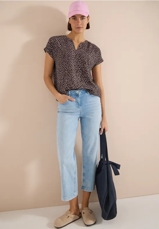 Femme porte un top à motif manches courtes, jean droit bleu clair, mocassins beiges et un sac fourre-tout bleu marine.