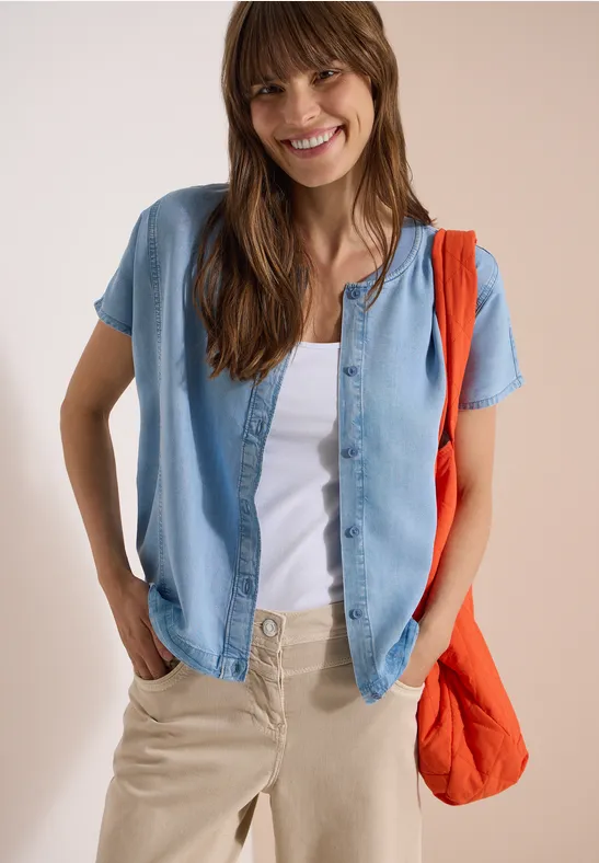 Persoon draagt een wit t-shirt, een open spijkerblouse, een beige broek en een oranje schoudertas.