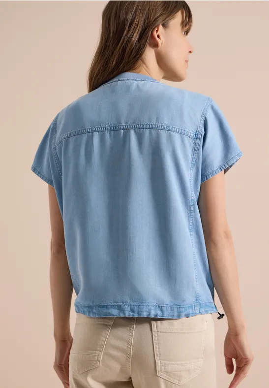 Vrouw van achteren in een lichtblauw denim kort mouwen overhemd en beige broek.
