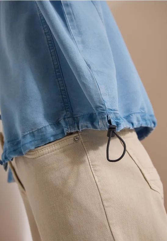 Zijaanzicht van een persoon in beige broek en blauw bovenstuk met trekkoord aan de zoom.