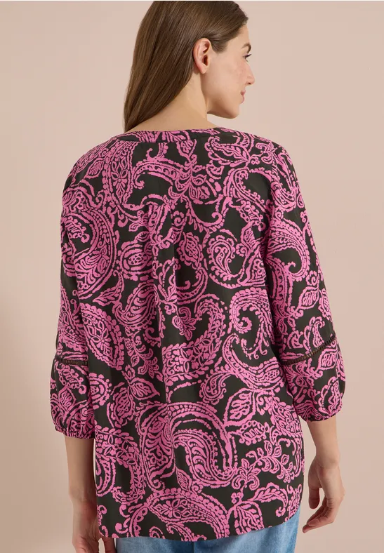 Vrouw van achteren in een blouse met roze-zwarte paisleyprint.