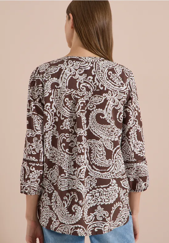 Vrouw van achteren in bruine blouse met wit paisleymotief.