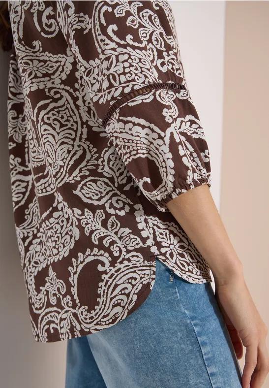 Zijdelingse opname van een bruin hemd met wit paisleypatroon en blauwe jeans.