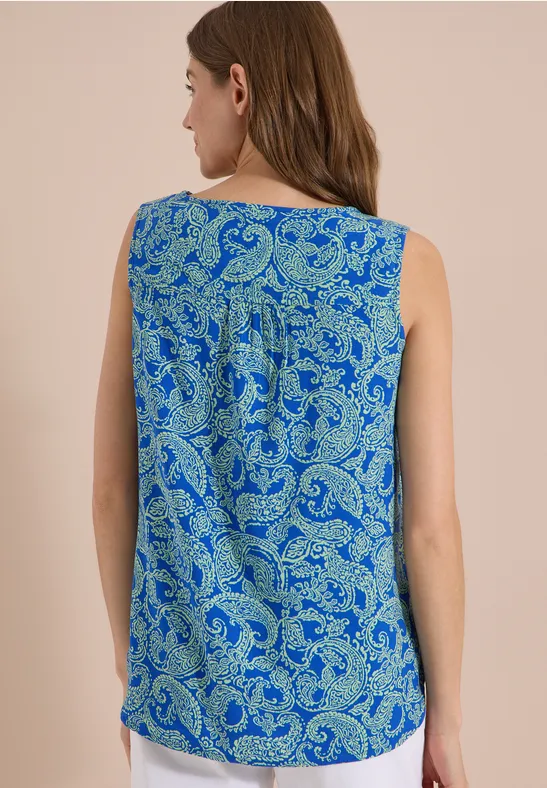 Rückansicht einer Frau in ärmellosem Top mit blau-grünem Paisley-Muster.