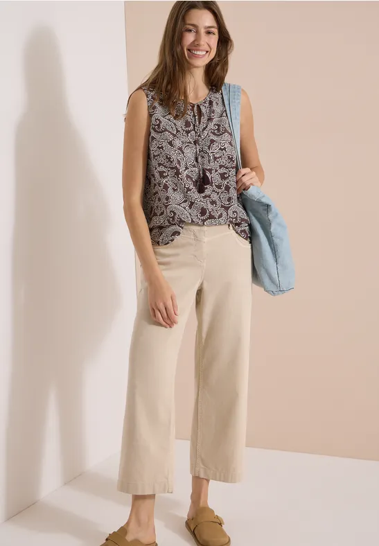 Femme en top sans manches à motifs, pantalon ample clair et sac à main bleu.