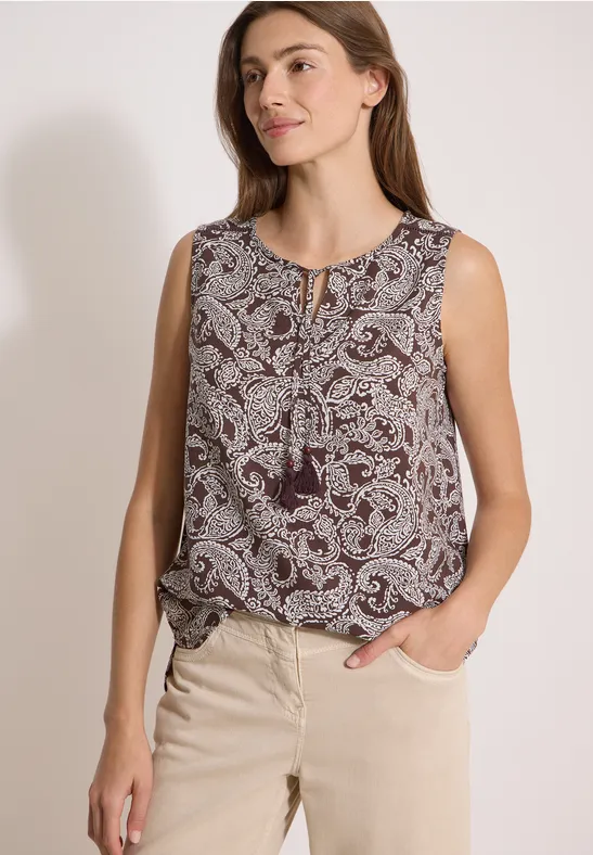 Femme en haut sans manches à imprimé cachemire et pompons, portée avec un pantalon beige.