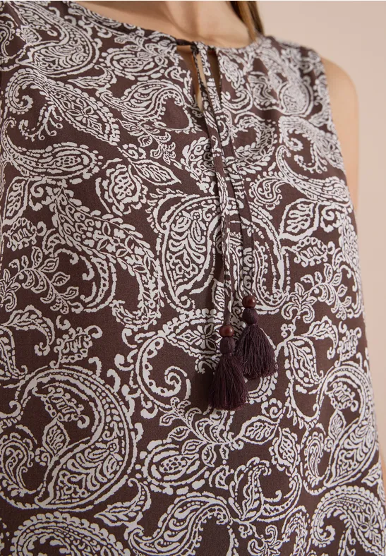 Top marron sans manches à motif paisley blanc avec pompons au niveau de l'encolure.