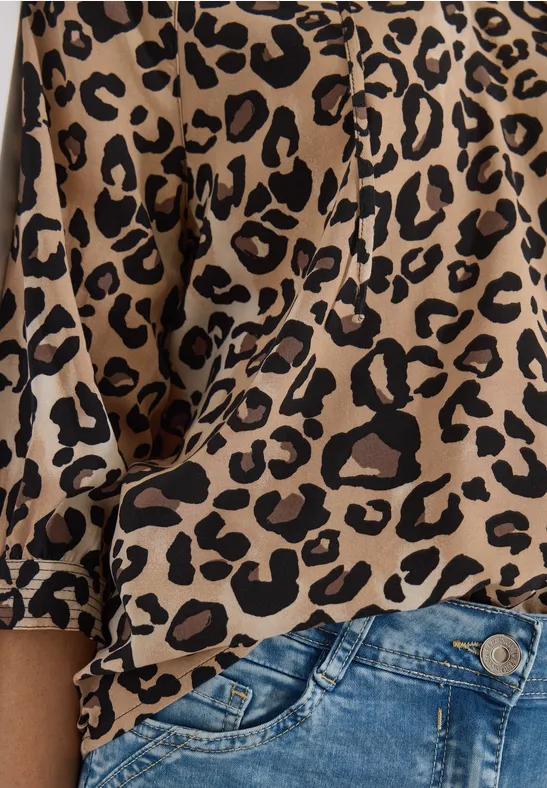 Eine Person trägt eine Leopardenmuster-Bluse und blaue Jeanshose.