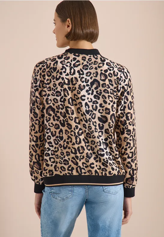 Rückansicht einer Person in leopardgemusterter Jacke mit schwarzem Saum und hellblauen Jeans vor beigem Hintergrund.