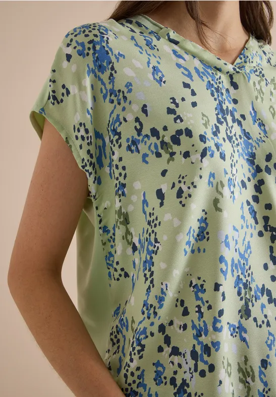 Eine hellgrüne Bluse mit abstrakten blauen Tupfen.