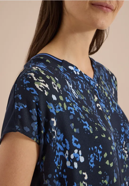 Gros plan sur une femme portant un haut bleu marine à manches courtes et motifs colorés, col en V.