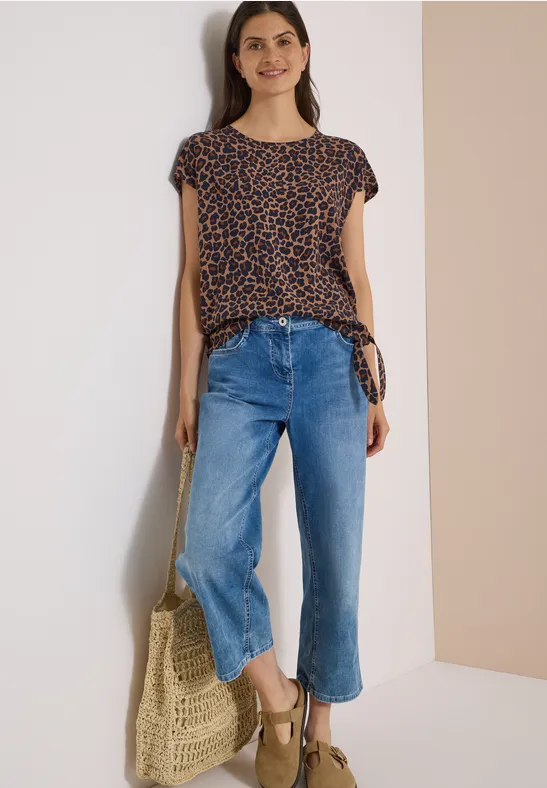 Eine Frau trägt ein gepunktetes Shirt, weite blaue Jeans, Keilsandalen und hält eine geflochtene Tasche.