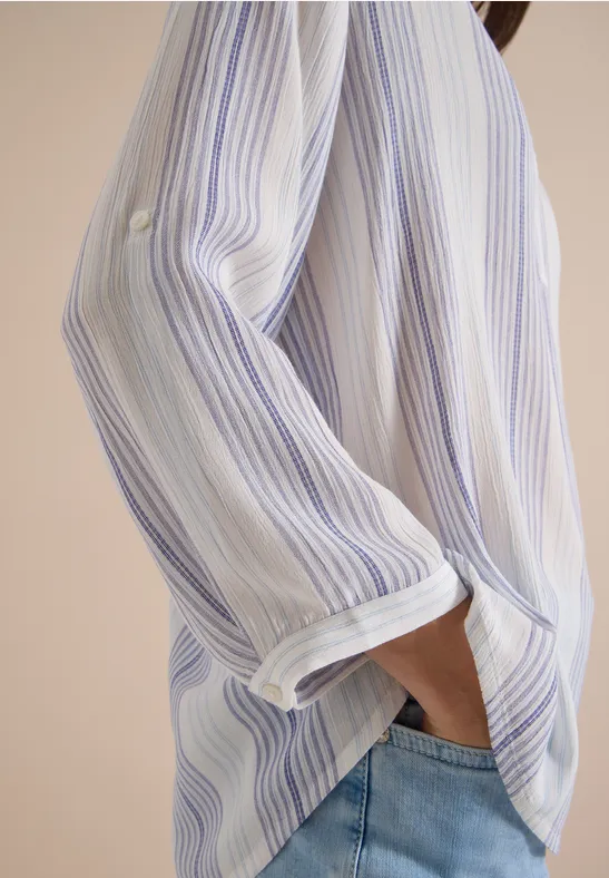 Vue de côté : une personne porte une chemise rayée bleu et blanche, main dans la poche de son jean