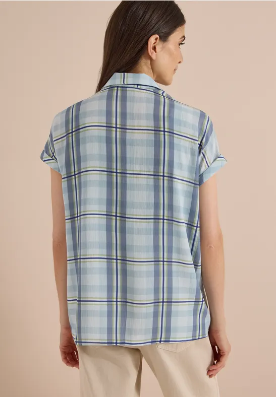 Vue de dos d'une femme portant une chemise à carreaux bleu clair et un pantalon beige.